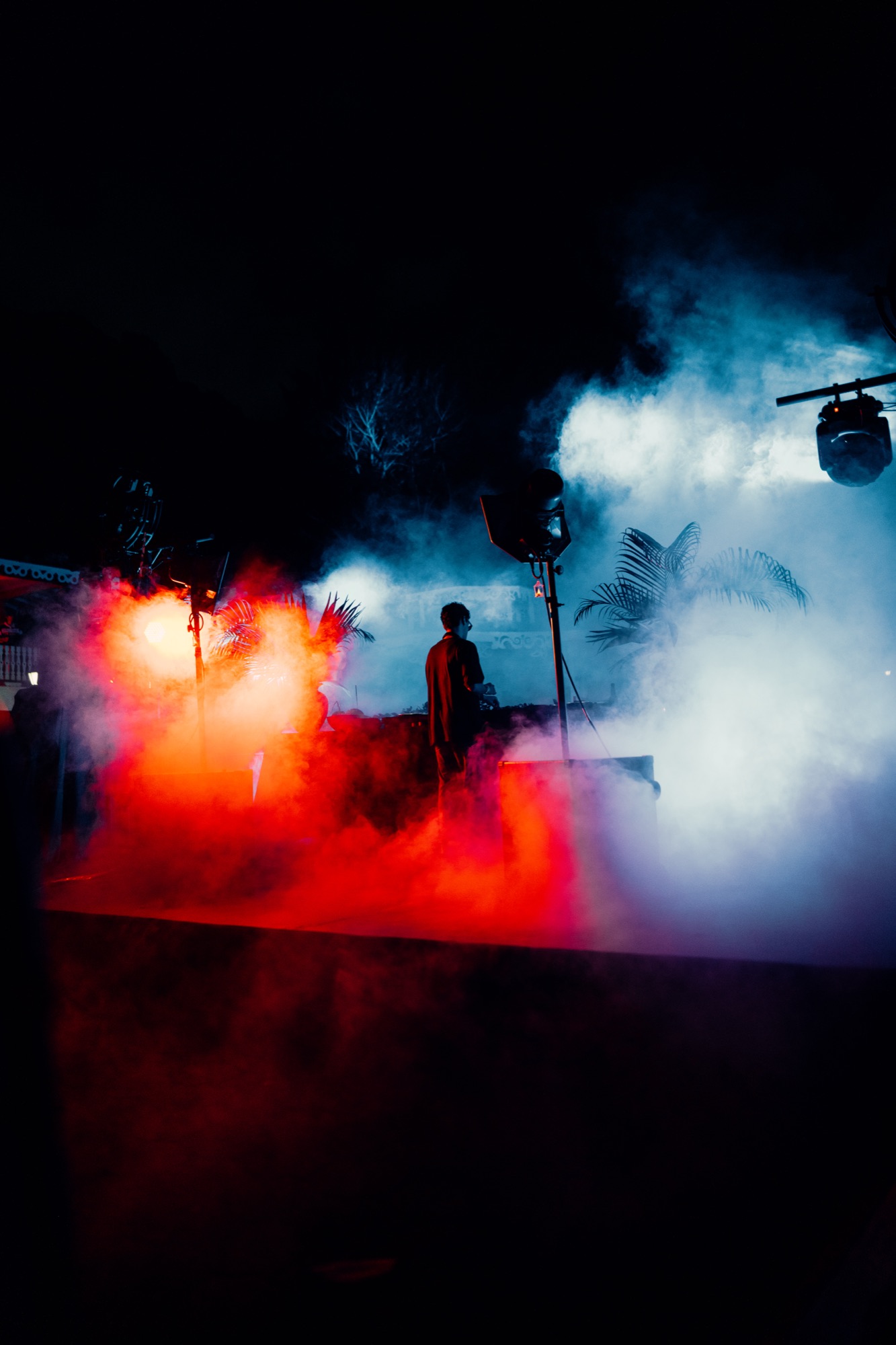 Silhouetted DJ surrounded by red and blue stage fog